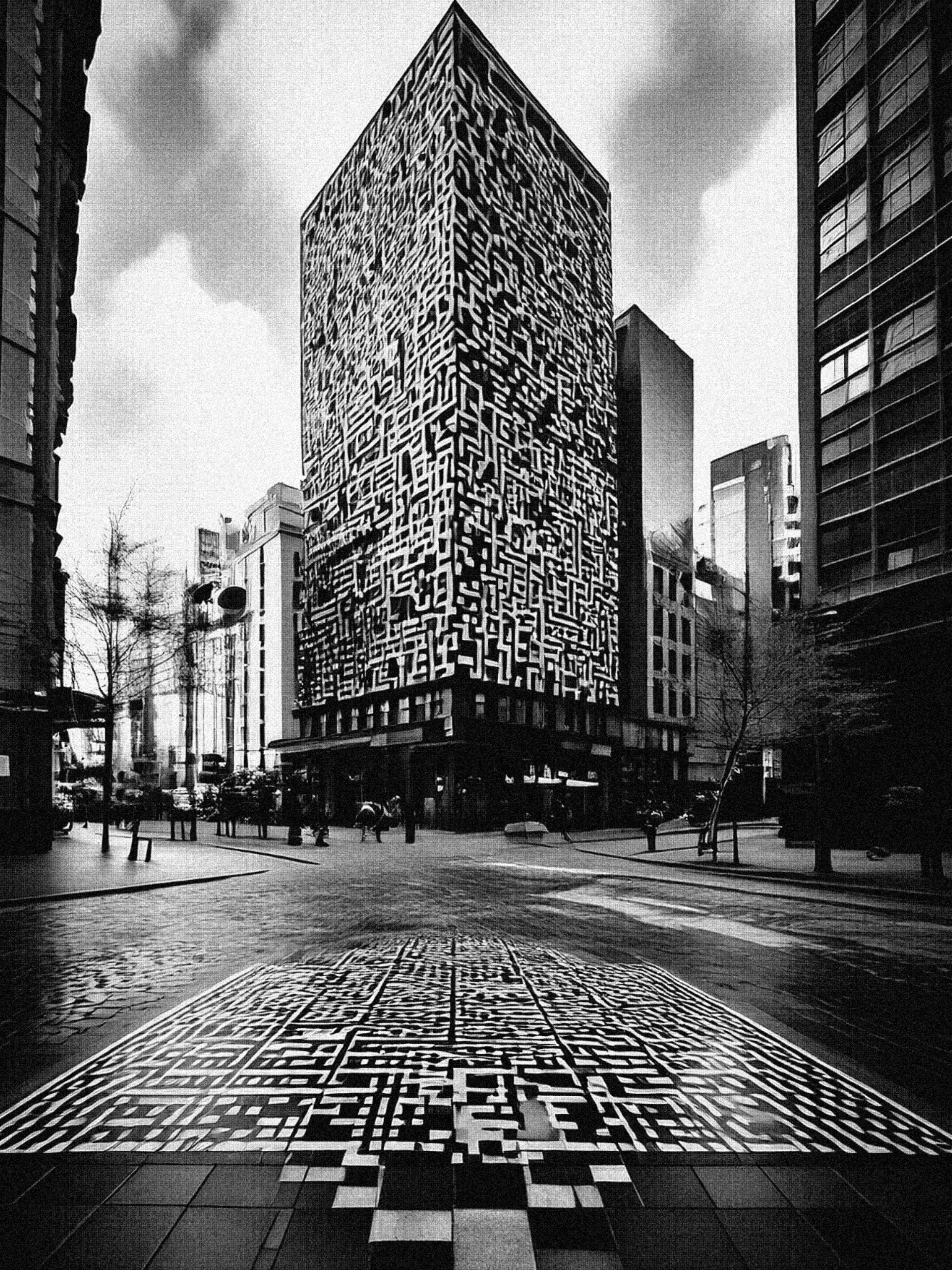 The black and white image shows a city scene with a large sky scraper in the middle. Embedded on the large tower building is a QR code pattern in white. In the paved road leading to the block is also a QR code like pattern. The street is fairly empty in the city with a few trees lining the side walks. The shot is taken from a low angle, so it as if the user is looking up to the tower block building. 